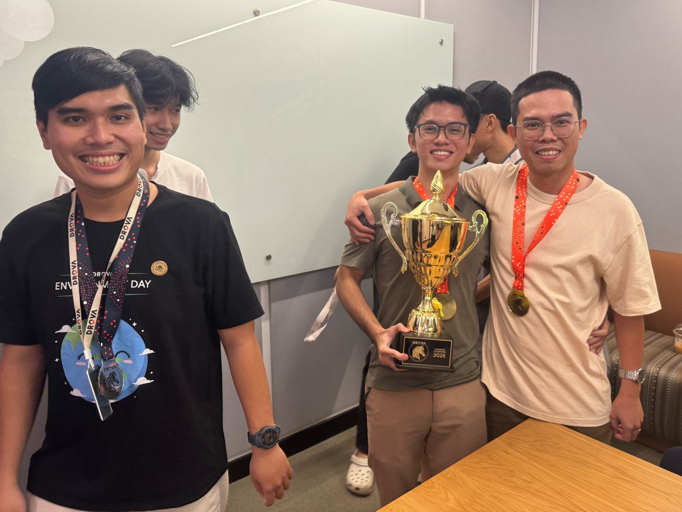 Four Drova colleagues in Ho Chi Minh City celebrating, two holding the gold Stampede Champions trophy and wearing medals