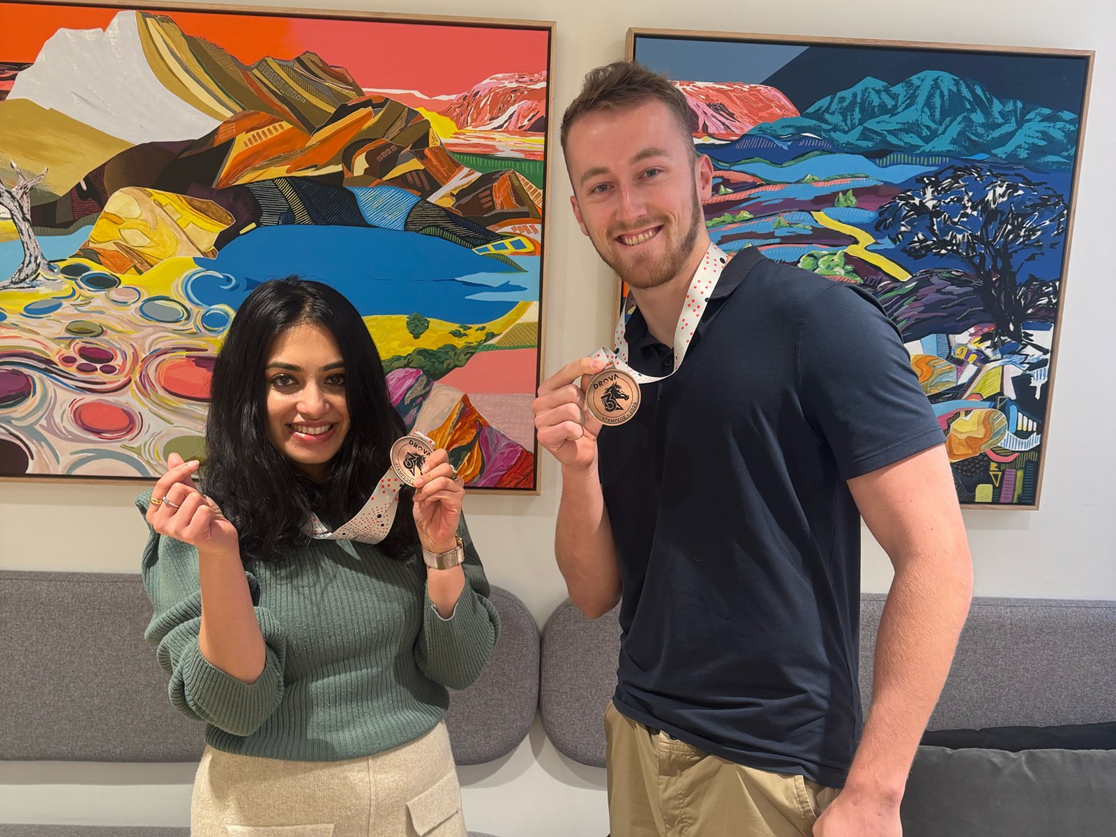 Two Drova colleagues in the Sydney office smiling and holding up their Drova Stampede 2025 medals
